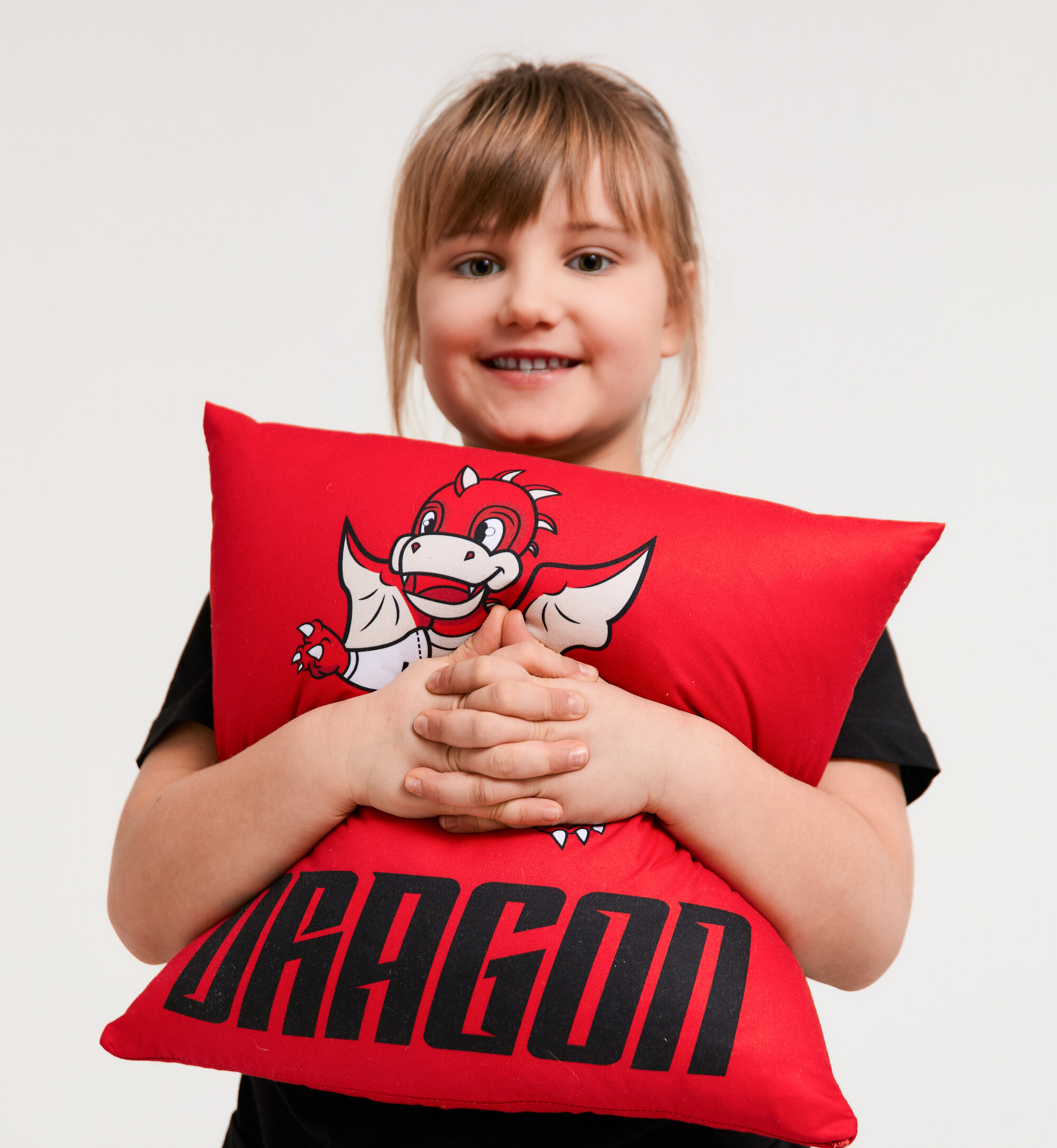 Dziewczynka w koszulce klubu przytula poduszkę z Dragonkiem