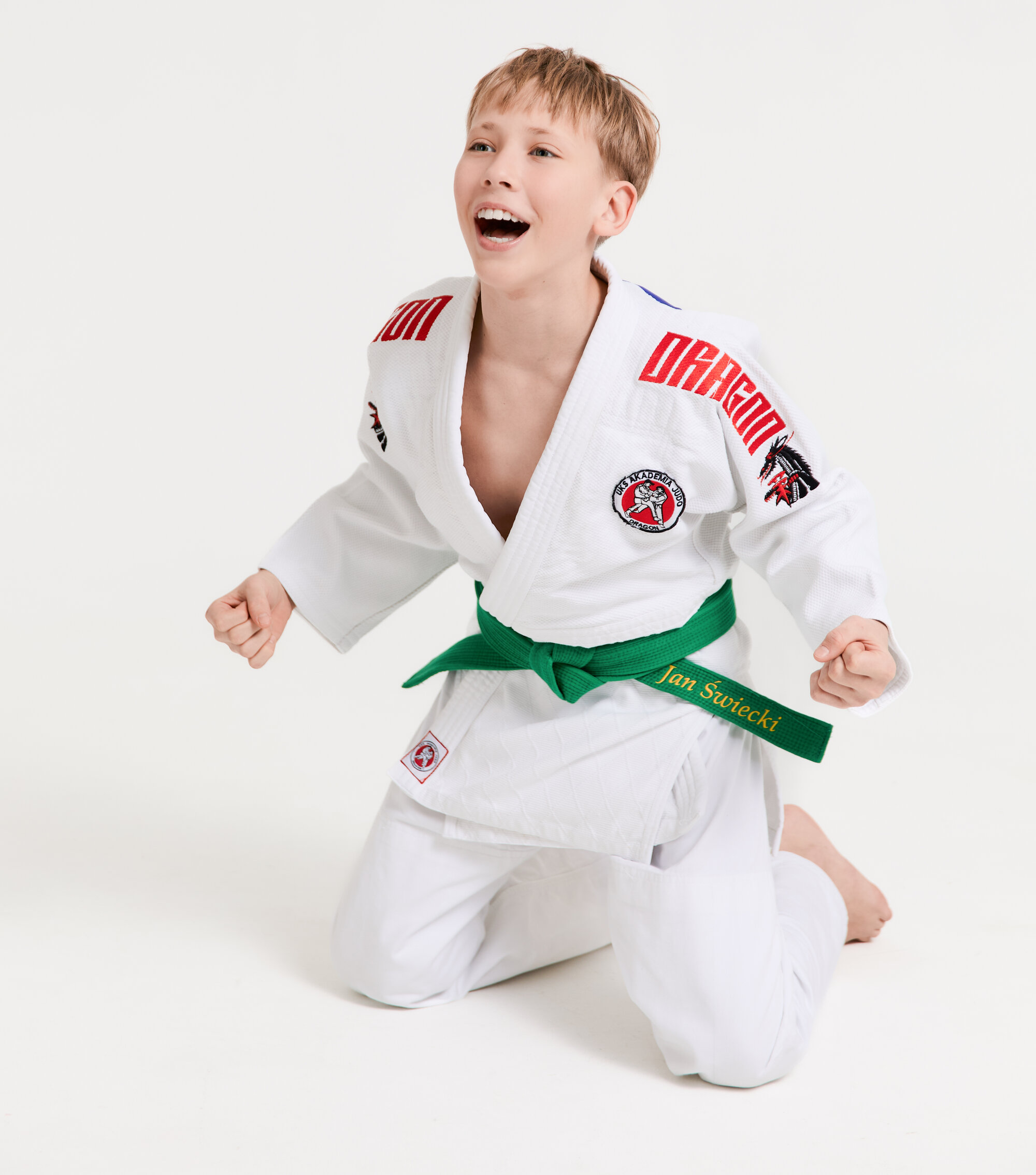 Chłopiec w judogi Akademii Judo Dragon z zielonym pasem, na kolanach, z okrzykiem radości