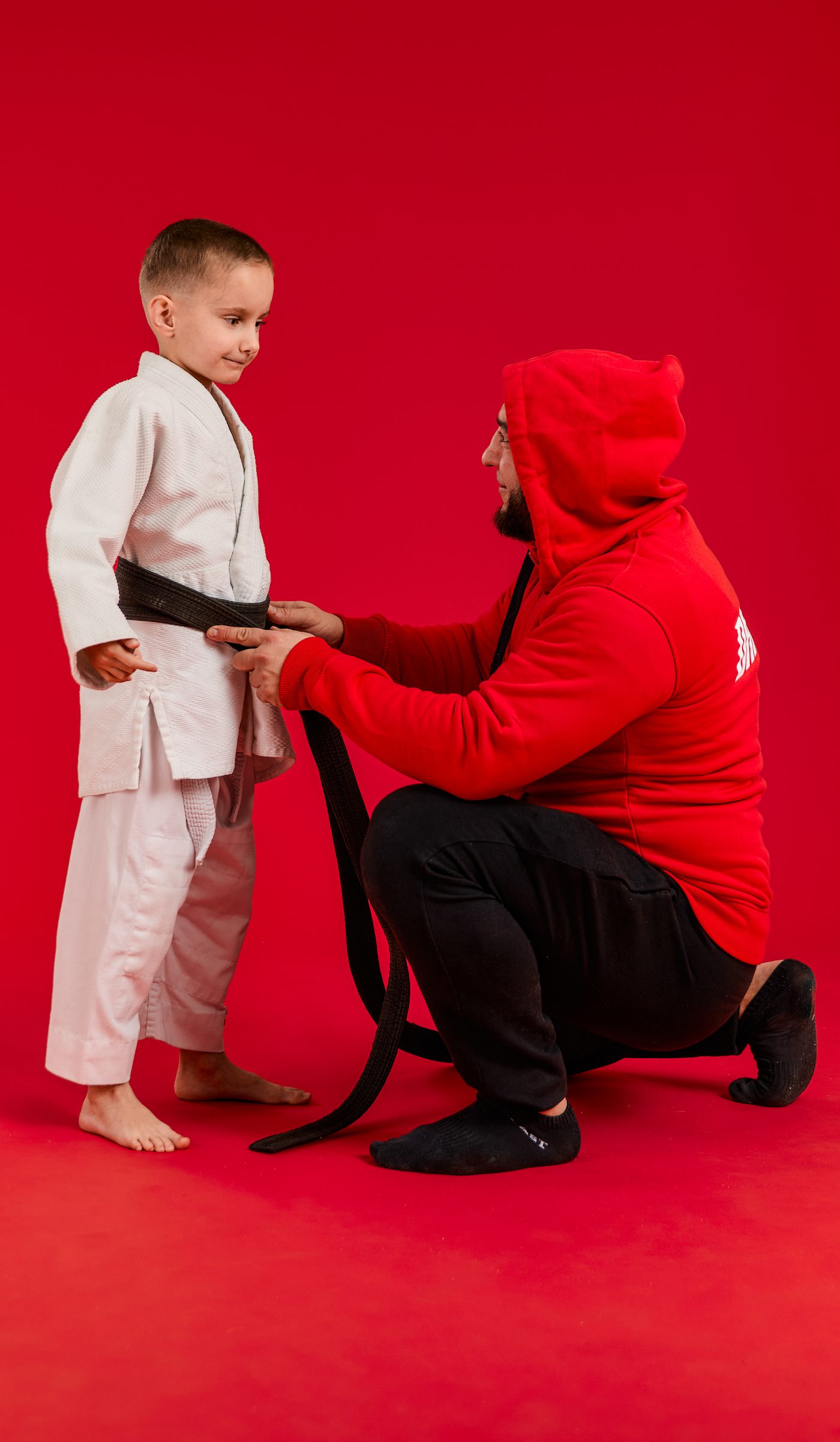 Trener kuca przy chłopcu w judodze i wiąże mu pas