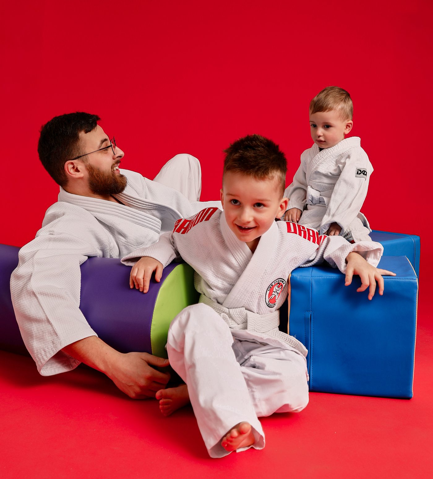 Trener Akademii Judo Dragon siedzi na macie wśród roześmianych przedszkolaków